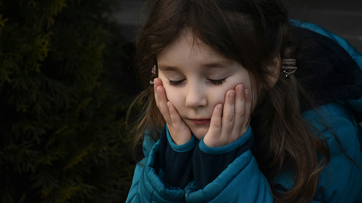 Sad young girl wearing a blue jacket with hands on cheeks, reflecting trust issues with family blacklisted local babysitters