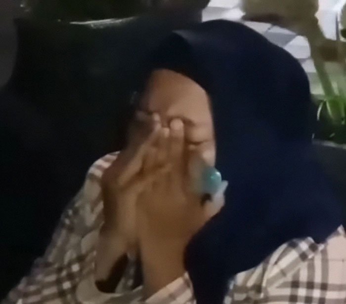 A person in a dark headscarf covering their face with hands, showing grief after Bali ferry sank with missing people.