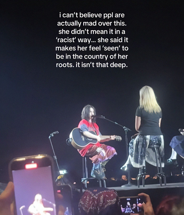 Billie Eilish performing on stage with a guitar during a concert amid controversy over a comment deemed racist.