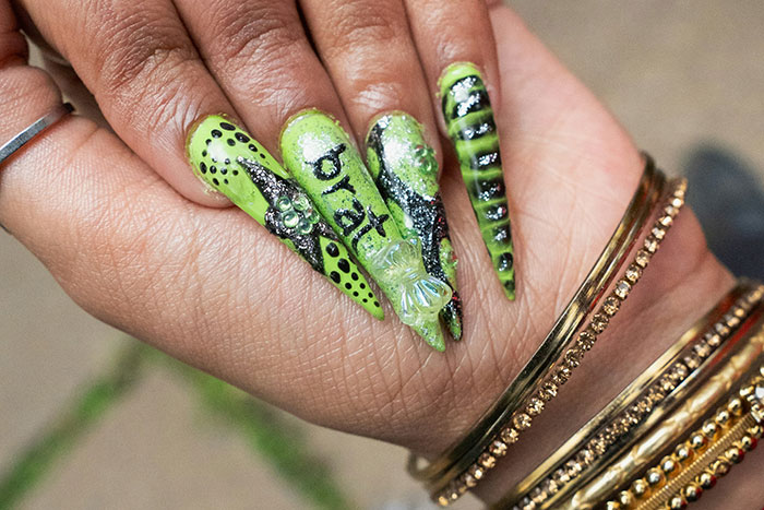 Close-up of long, green, black-accented nails showcasing bold fashion trend propaganda and unique nail art designs.