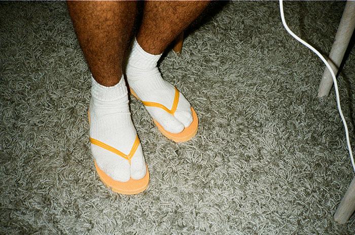 Legs wearing white socks with orange flip-flops on a textured gray carpet, rejecting a disliked fashion trend.