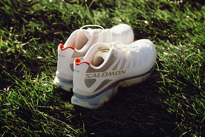 White Salomon sneakers on grass, highlighting a fashion trend many people refuse to follow or accept.