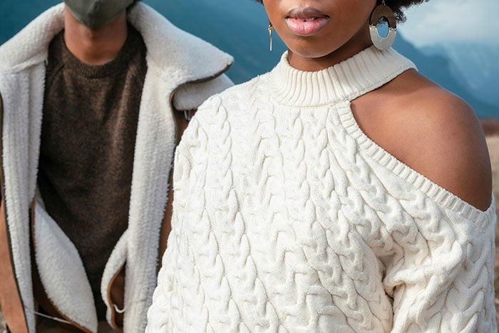 Two people wearing trendy winter fashion, featuring cable knit and shearling jackets amid outdoor natural scenery.