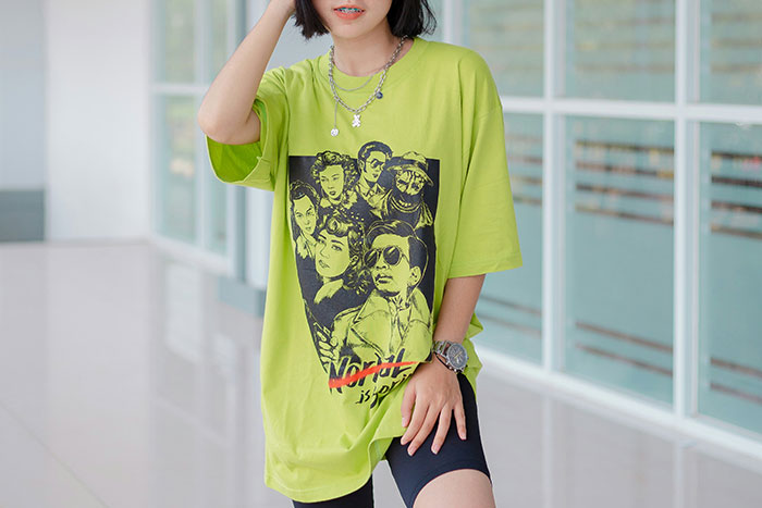 Young woman wearing oversized graphic t-shirt and layered necklaces, showcasing fashion trend propaganda style.