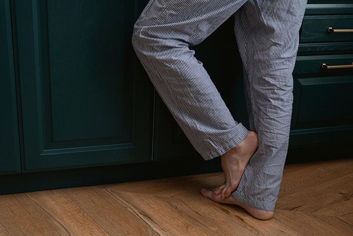 Person in striped pajama pants standing barefoot on wooden floor against dark cabinets, illustrating fashion trend rejection.