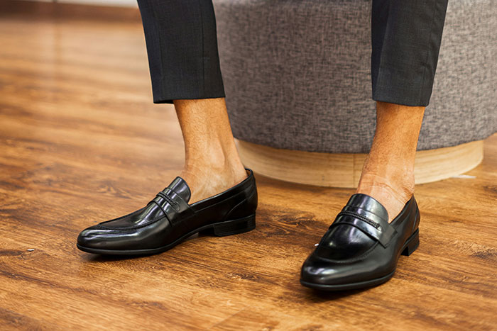 Close-up of a person wearing black leather loafers and cropped pants, highlighting a fashion trend they refuse to follow.