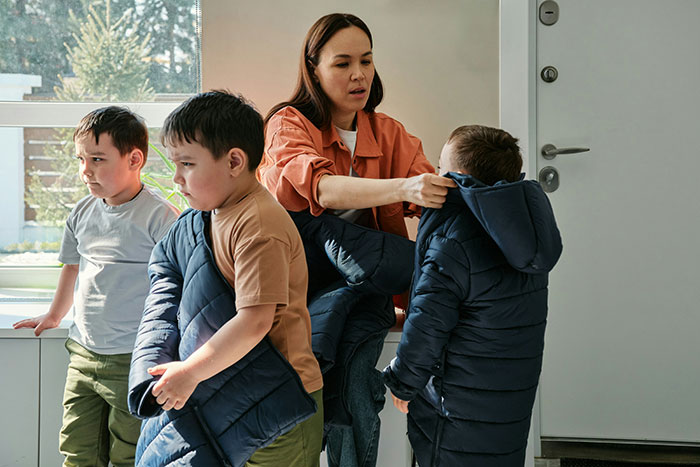 Woman helping children put on jackets inside a home, illustrating a job experience where people went home on the spot.