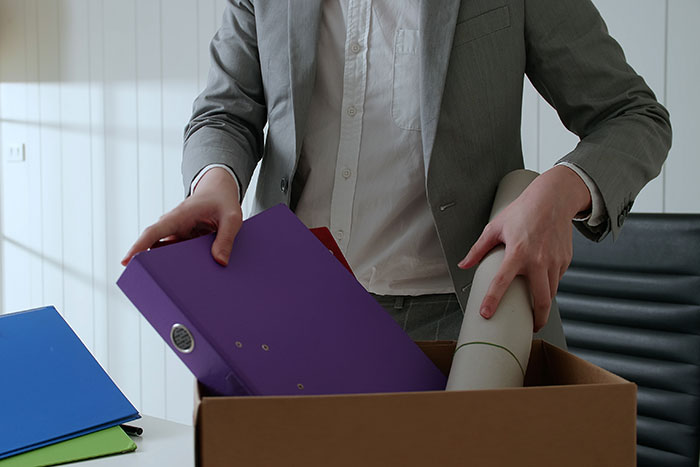 Person in a suit packing a box with office files and documents, symbolizing quitting a job experience immediately.
