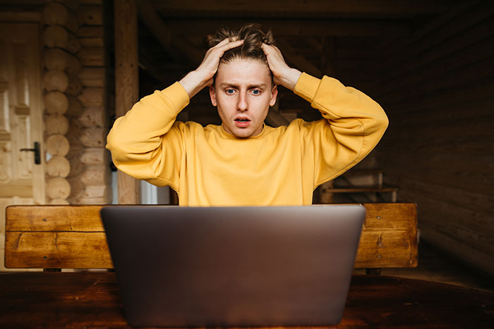 Young man in yellow sweatshirt looks shocked at laptop, reflecting a horrific job experience and quick quitting decision.