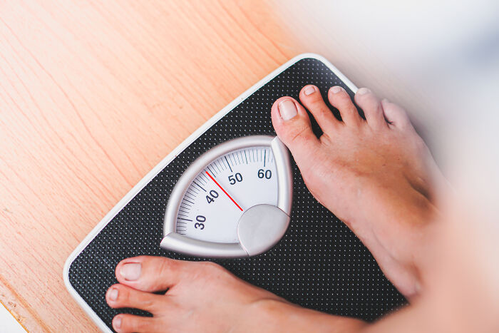 Person standing barefoot on an analog scale showing weight, related to weird things and terrifying details with dead bodies.