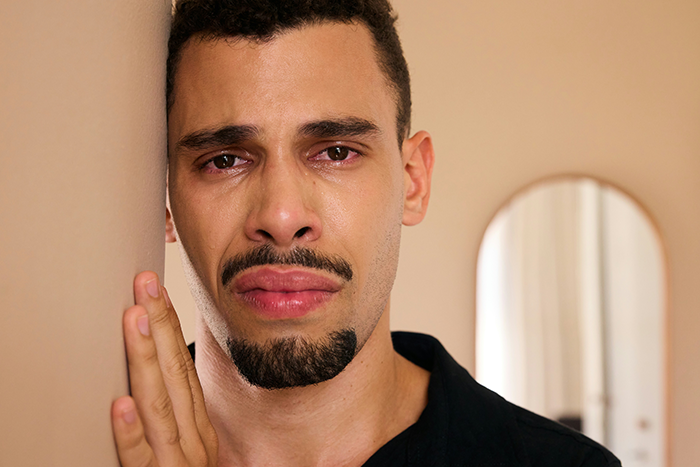 Man with a tearful expression leaning against a wall, depicting emotions related to cheating accusation and DNA test forgiveness. - 18