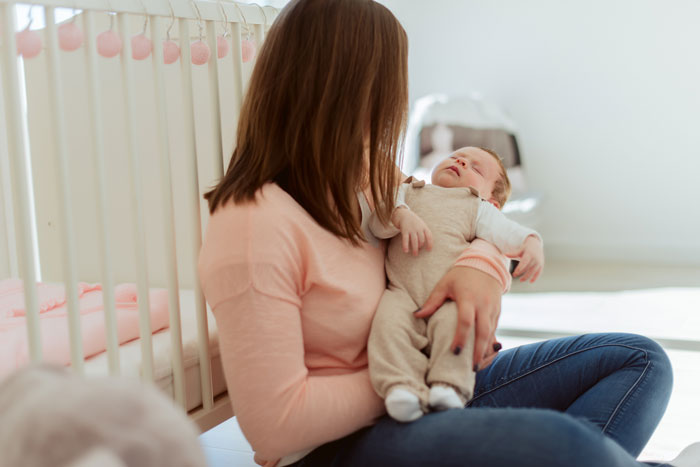 Woman sitting on the floor holding a sleeping baby near a crib, illustrating grandpa skipping babysitting duty and family tension. - 7