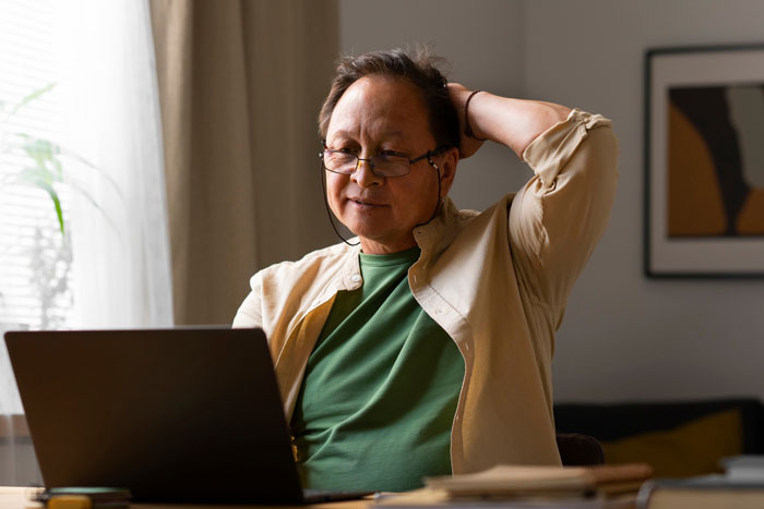 Grandpa using laptop at home, looking frustrated as he skips babysitting duty for party weekend plans. - 24