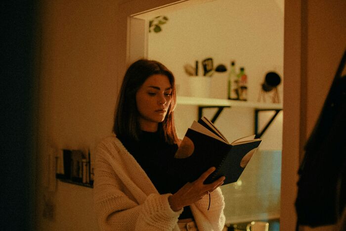 Woman in cozy sweater reading a book indoors, reflecting on the pettiest things that cause breakups borderline insane.