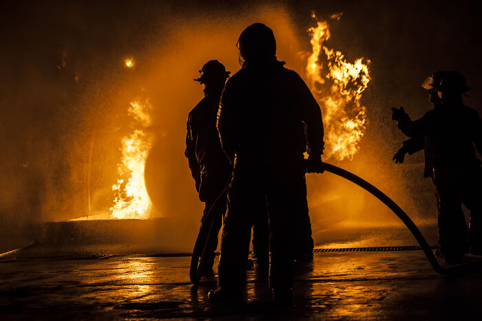 Silhouettes of people handling a hose near large flames, depicting intense moments related to dealing with dead bodies.