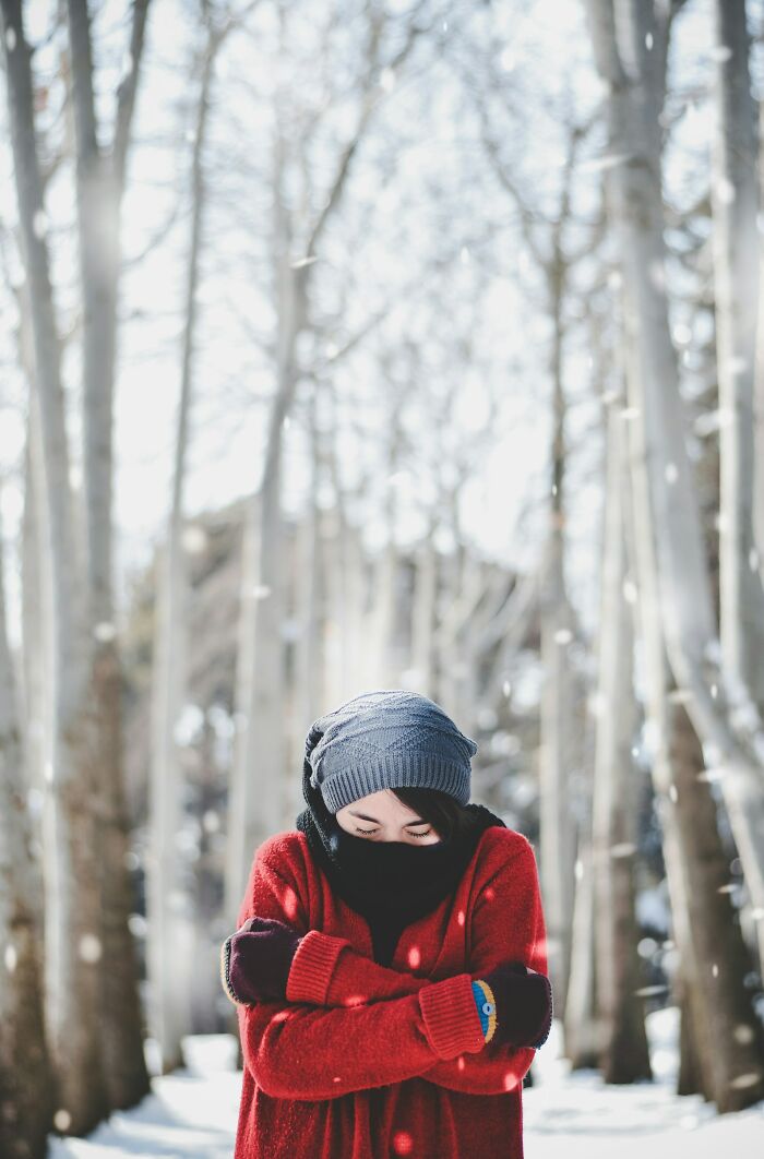 Person wearing winter clothes shivering in a snowy forest illustrating survival tips that won't help you at all concept.