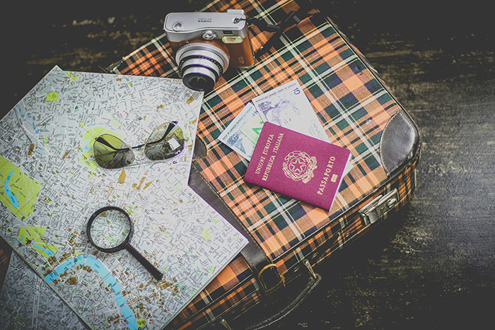 Travel essentials on vintage suitcase including map, sunglasses, camera, and passport highlighting vacation planning and trip backlash.