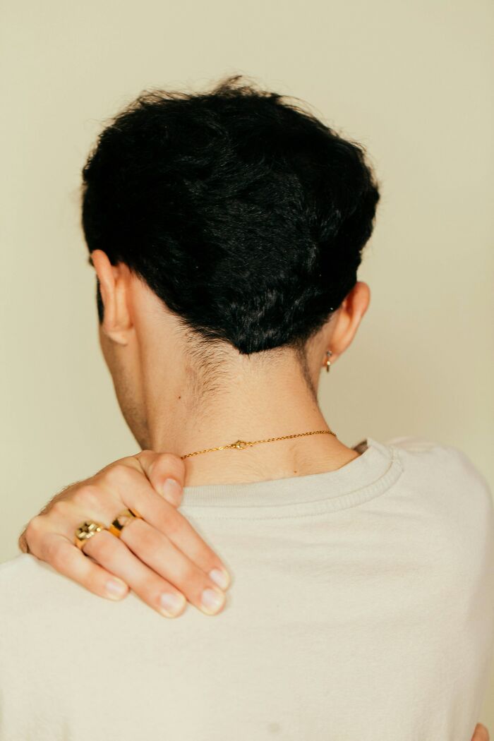 Person wearing gold chain and rings touching their neck seen from behind, illustrating entitled patients demanding special treatment.