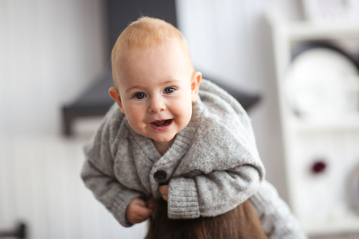 Smiling baby in a gray sweater being held, illustrating the theme of woman choosing to be a single mom and babysitting challenges. - 5