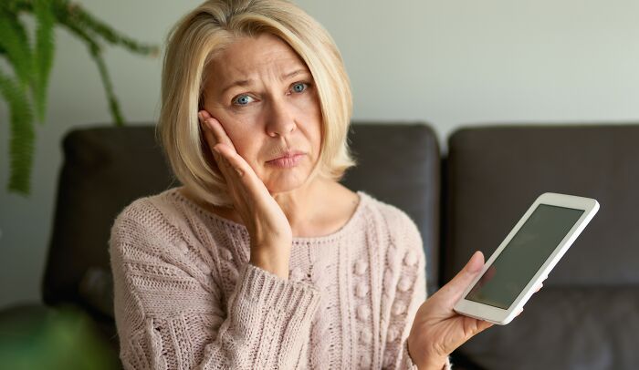 Middle-aged woman looking upset while holding a smartphone, reflecting on a rude comment from a 23YO. - 16
