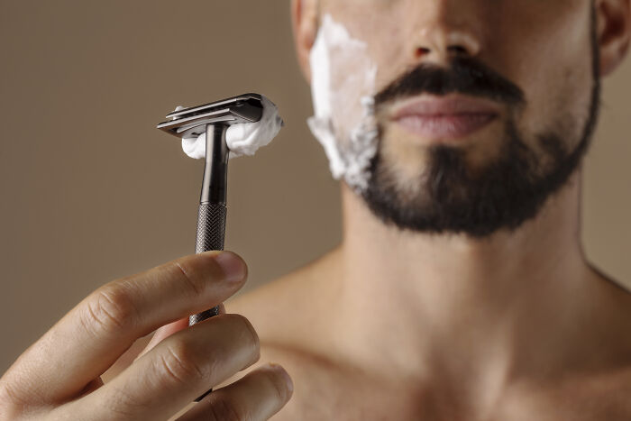 Close-up of a man holding a razor with shaving cream on his face, illustrating truckers share craziest things seen. - 30