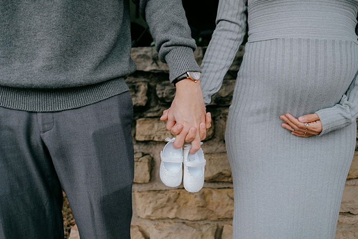 Pregnant fianc&eacute;e holding baby shoes while couple holds hands, symbolizing teen sabotaging dad's relationship.