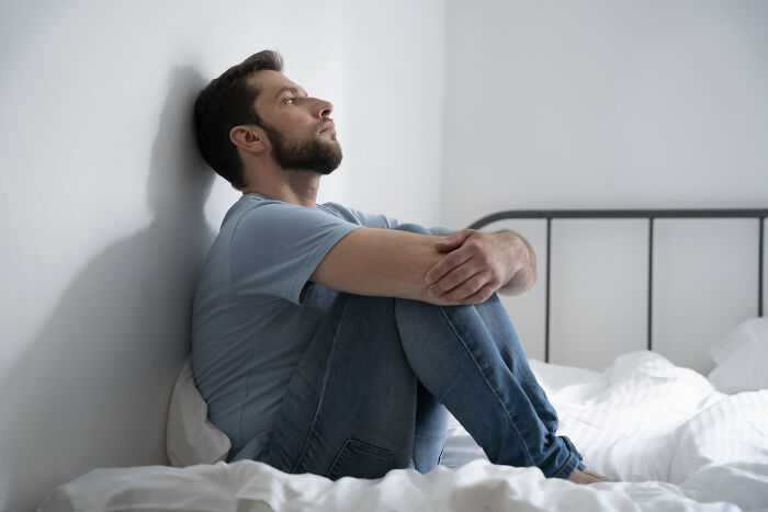 Young man sitting on bed, looking thoughtful and reflective, relating to unhinged pieces of family lore.