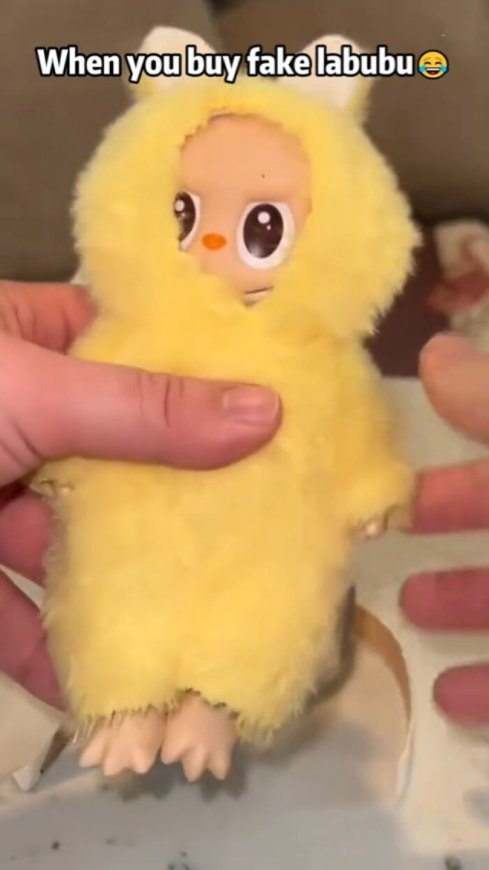 Hand holding a fake Labubu doll in a yellow fuzzy costume, highlighting creepy and nightmarish fake Labubus.