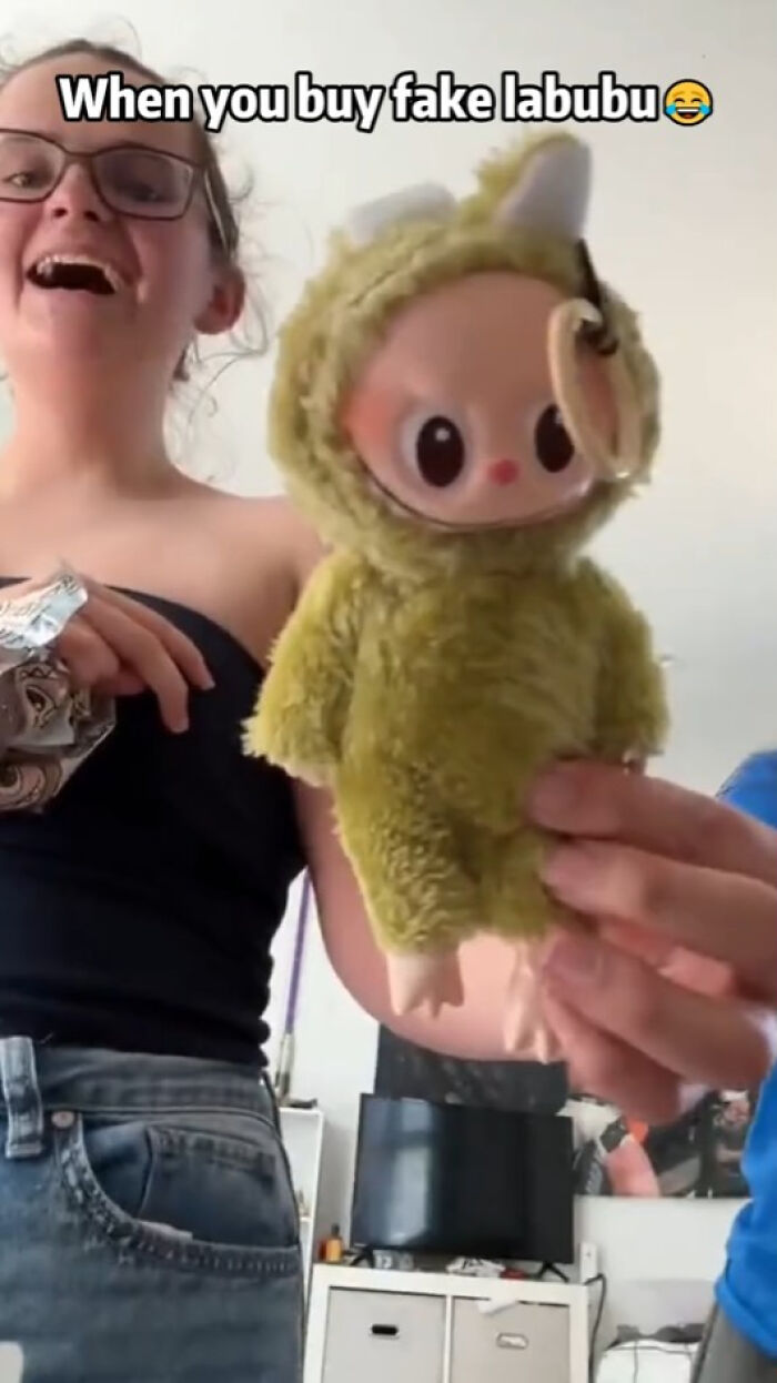 A person holding a fake Labubu doll in a fuzzy costume, with text about buying fake Labubu toys.