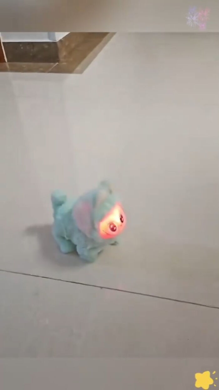 A small plush toy with a glowing, eerie face walking on a tiled floor resembling creepy fakes.