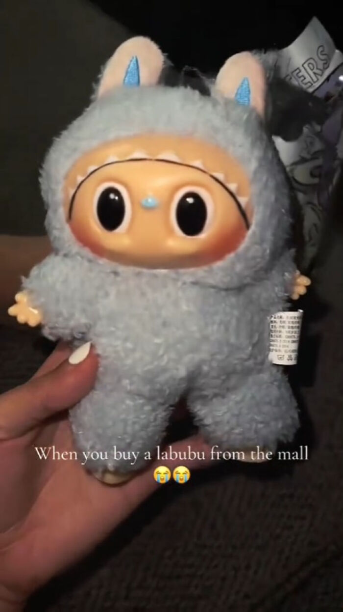 Close-up of a creepy Labubu fake doll with large eyes and fuzzy costume held in hand at night.