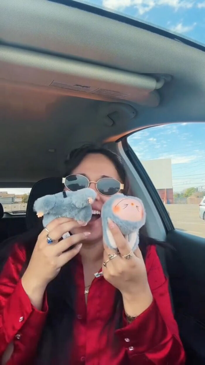 Woman in sunglasses holding two creepy Labubus fakes inside a car on a sunny day.