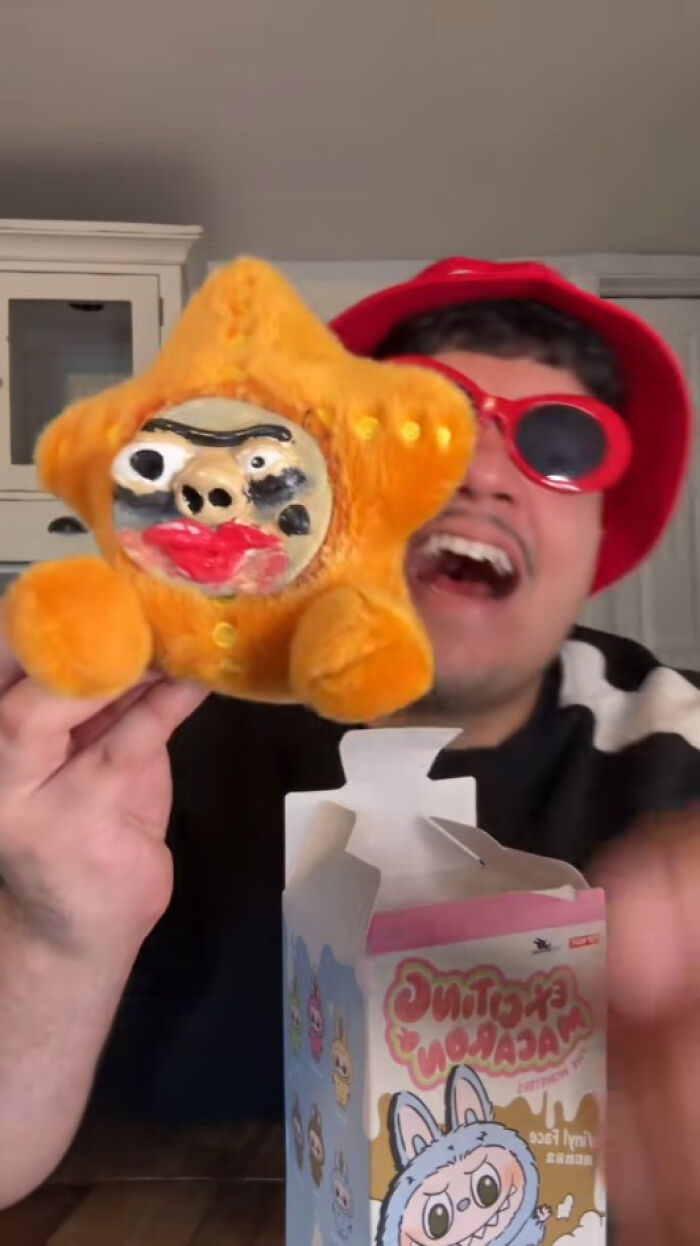 Person holding a creepy fake Labubus plush with distorted face next to its original packaging box indoors.