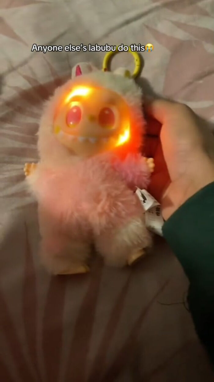 Glowing creepy Labubu doll held by hand, fuzzy pink body with illuminated face, eerie toy giving nightmares.