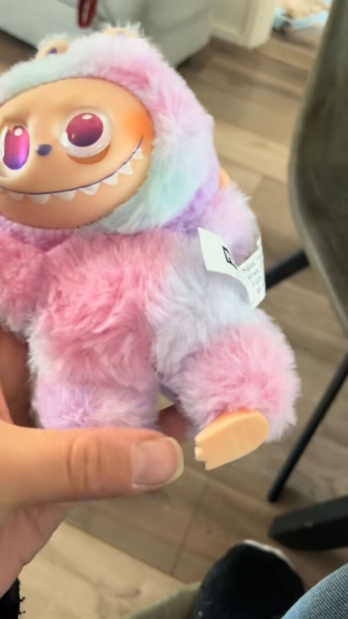 Hand holding a creepy Labubus fake toy with bright eyes and pastel fur, evoking a nightmarish vibe.