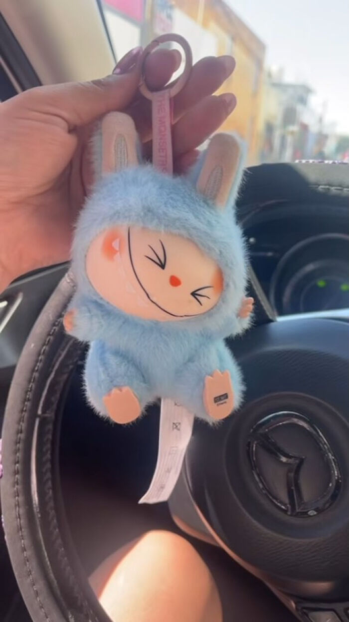 Hand holding a creepy Labubus plush keychain inside a car, highlighting Labubus fakes that might give nightmares.