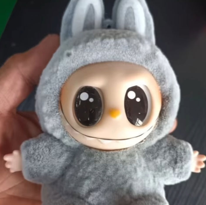 Creepy Labubus fake doll with large eyes wearing a fuzzy bunny costume, held in a hand.