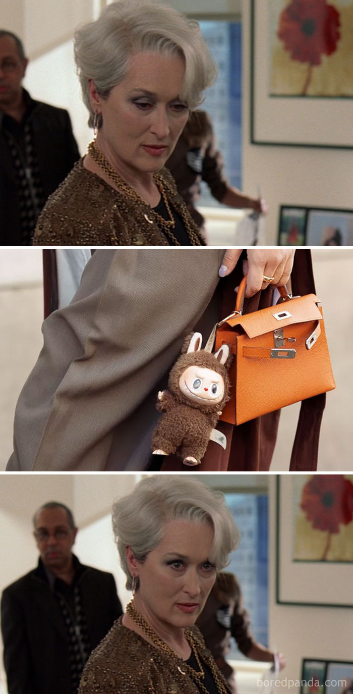 Woman with silver hair looking serious, holding an orange purse with a Labubu doll keychain attached.