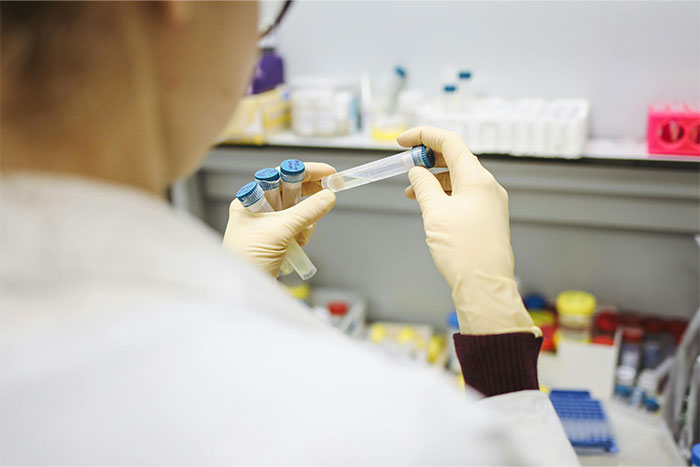 Laboratory technician holding test tubes with blue caps in a scientific research setting for legal case evidence analysis.