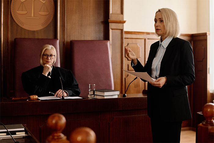 Female lawyer presenting a case in court with judge listening attentively in a wood-paneled courtroom setting.