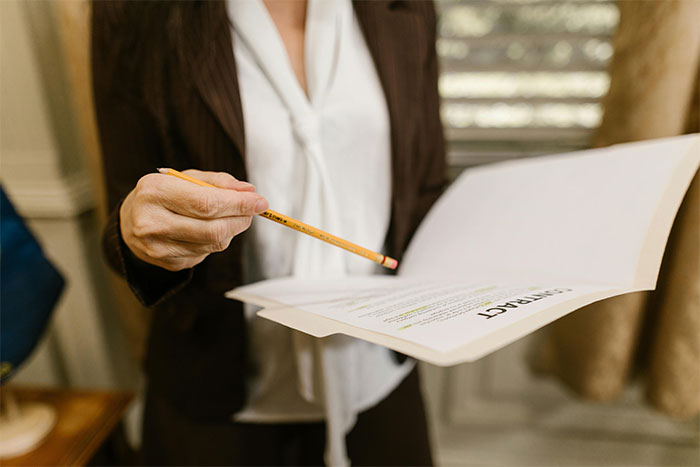 Person holding contract and pointing with pencil, illustrating lawyers and defendants failing miserably in court situations