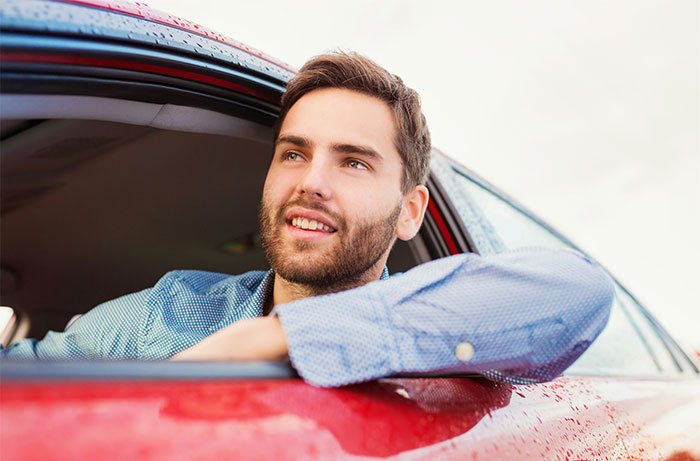 Man with beard leaning out of red car window, smiling and looking away, symbolizing lawyers and defendants failing in court.