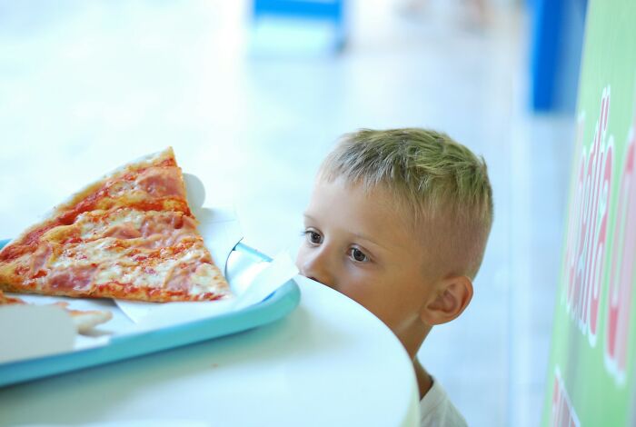 Young boy looking longingly at a slice of pizza on a table, illustrating harsh parenting and punishment of kids.