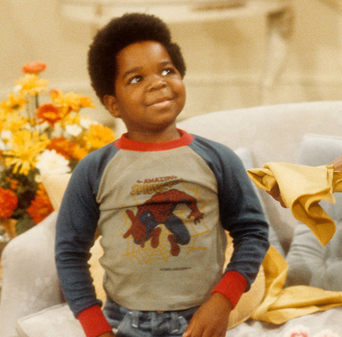 Young Gary Coleman smiling and wearing a Spider-Man shirt in a cozy living room setting with flowers in the background Young Gary Coleman smiling and wearing a Spider-Man shirt in a cozy living room setting with flowers in the background