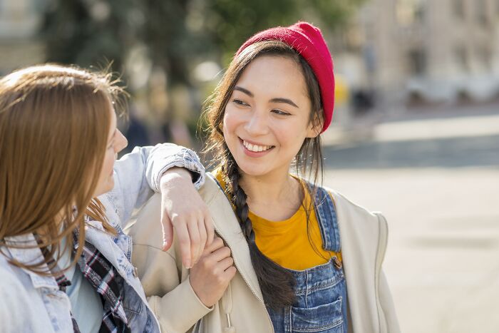 Two young women smiling and sharing Gen Z compliments outdoors on a sunny day, showing friendly connection.
