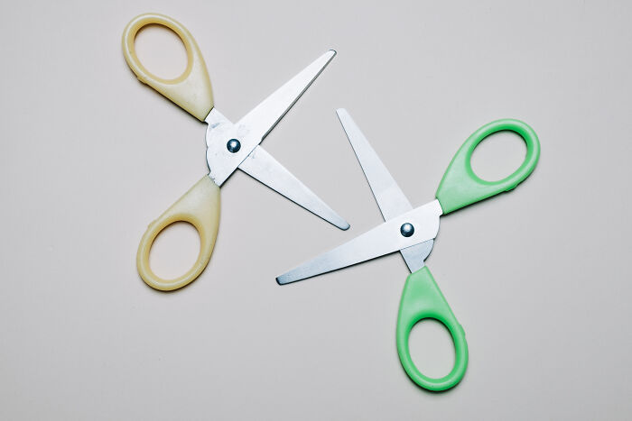 Two pairs of scissors with beige and green handles placed on a light surface, illustrating outlandish Gen Z compliments.