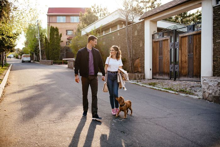 Young couple walking dog on sunny street, showcasing Gen Z style and outlandish ways to hand out compliments.