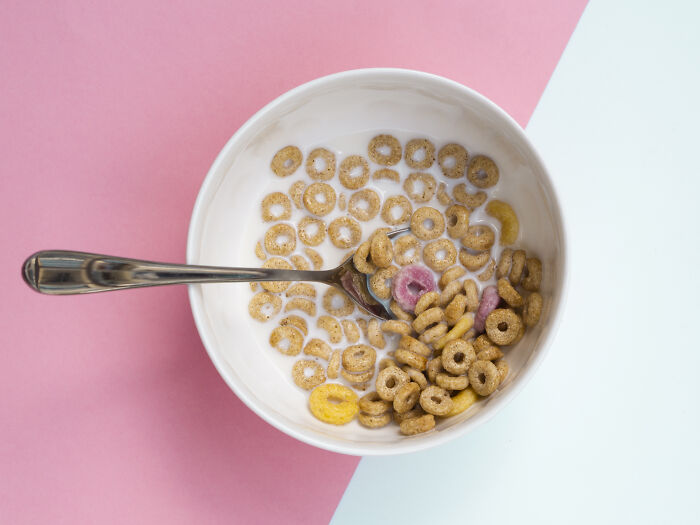Bowl of colorful cereal with milk and a spoon on a pink and light blue background representing Gen Z compliments.