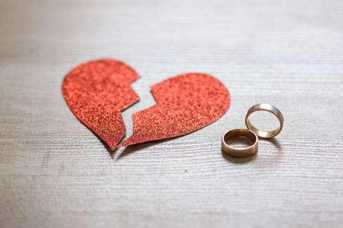 Broken red glitter heart next to two wedding rings on a wooden surface symbolizing love and compliments