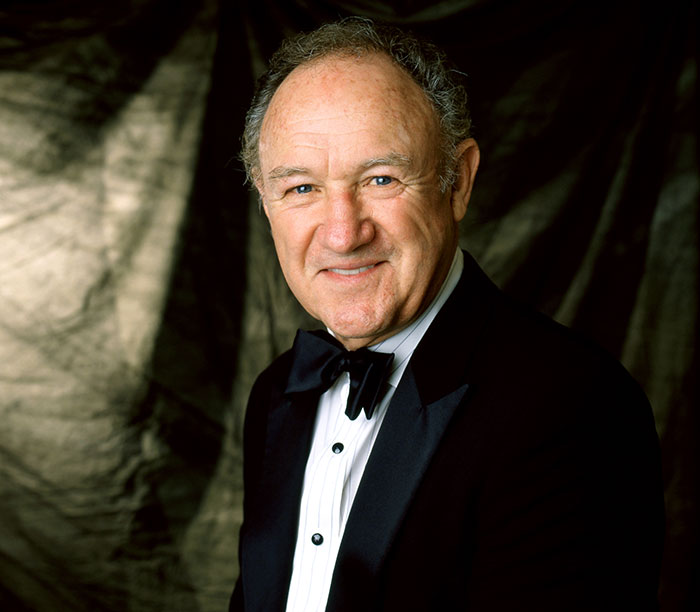 Elderly man in a tuxedo smiling against a dark backdrop, representing stars we've lost this year in July.